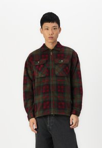 Rot und grün karierter Flanelljacke mit einem Frontreißverschluss, zwei Brusttaschen und einem Kragen. Weicher Stoff und entspannte Passform.