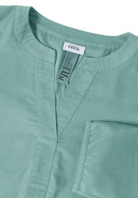 Camicia in velluto a coste verde chiaro con scollo a V arrotondato e etichette cucite con la scritta "CECIL" e "JOYFUL."