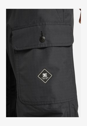Schwarze Cargo-Hose mit einem strukturierten Rautenmuster. Verfügt über eine große Fronttasche mit Knopfverschluss und einem DC-Logo-Patch.