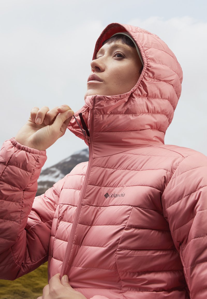 Giacca isolante rosa con cappuccio, caratterizzata da pannelli trapuntati e una cerniera anteriore, contrassegnata dal logo Columbia sul petto.