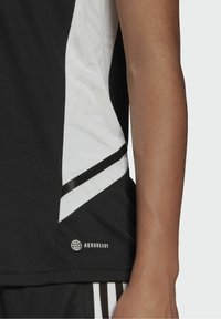 Černo-bílý atletický tričko s prodyšnou látkou, vzorovaným bílým bočním panelem a černým akcentem. Logo viditelné.