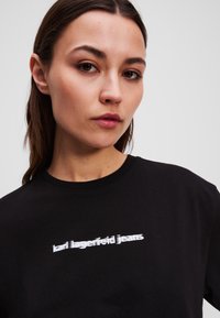 T-shirt noir à col rond et manches courtes, avec un logo brodé blanc portant la mention "karl lagerfeld jeans."