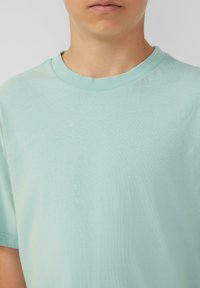 Licht muntgroene t-shirt met korte mouwen en een ronde hals, gemaakt van zachte, gladde stof. Eenvoudig ontwerp zonder zichtbare patronen of accenten.