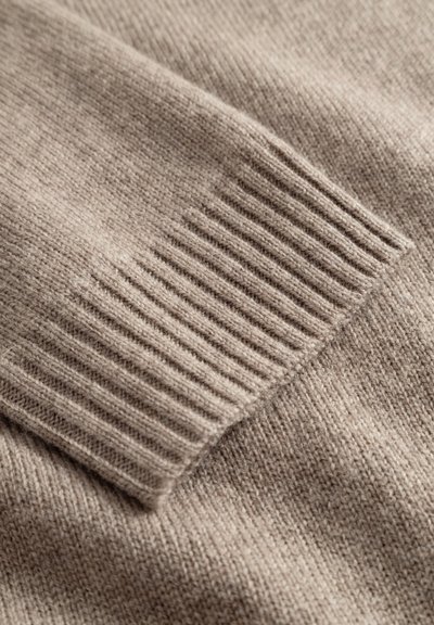 Tissu tricoté beige avec texture côtelée le long des bords, présentant une apparence douce et fine, mettant en valeur un tissage lisse et uniforme.