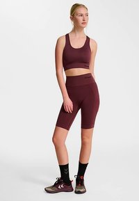 Burgundowy sportowy krótki top i krótkie spodenki rowerowe z wysokim stanem, wykonane z elastycznego materiału o gładkiej fakturze i minimalistycznym logo. Czarnych skarpetek i sportowych butów dopełniają wygląd.