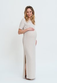 Abito premaman lavorato a maglia beige con maniche corte, spacchi laterali e una silhouette aderente, che migliora il comfort e la facilità durante la gravidanza.