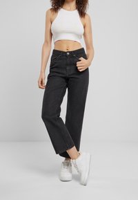 Jeans negros de tiro alto con un corte relajado, que cuentan con un cierre de botón frontal y cinco bolsillos. Combinados con una camiseta corta blanca y zapatillas blancas.