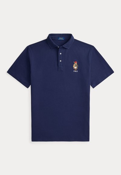 Polo azul marino de manga corta con cuello, tres botones y pequeño oso bordado que lleva un sombrero y bufanda rojos en el pecho izquierdo.
