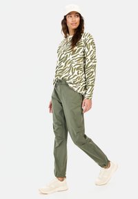 Langsleeve top in een groen en wit abstract patroon, gecombineerd met losse olijfgroene broeken en beige sneakers. Lichtgewicht stof.