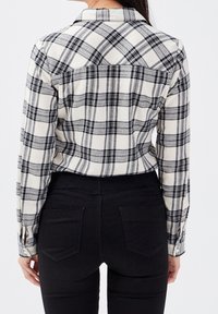 Chemise en flanelle à carreaux noir et blanc avec manches longues, col et détail du yoke arrière, associée à un jean noir ajusté.