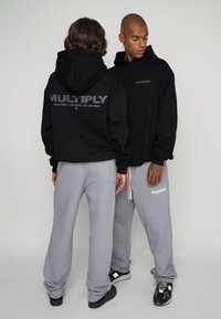 Black hoodies with "MULTIPLY" logo on back and front; paired with grey sweatpants; relaxed fit; soft fabric; minimal hardware details.