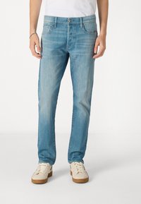 Ljusblå jeans med rak passform, har fem fickor, dragkedja och diskret blekning. Bärs med vita sneakers för kontrast.