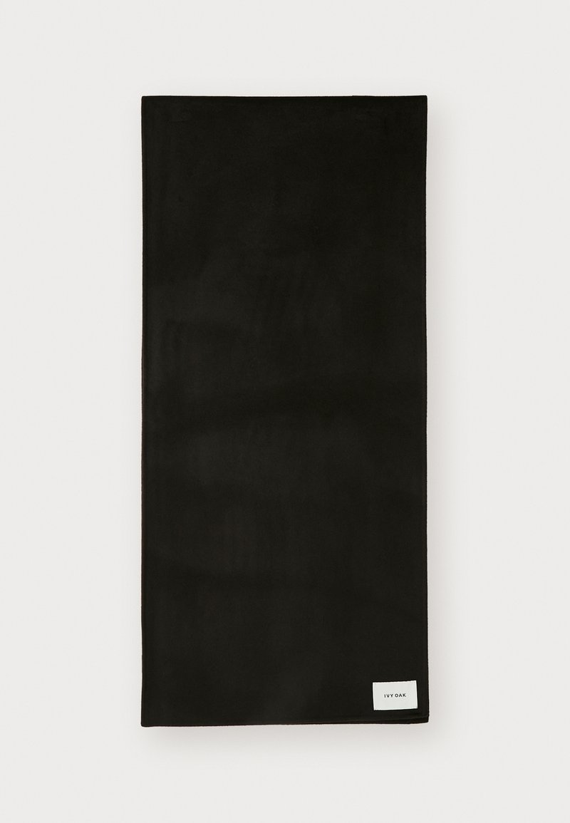 Asciugamano in tessuto nero con una consistenza liscia, forma rettangolare e una piccola etichetta bianca nell'angolo in basso a destra. Design semplice e minimalista.