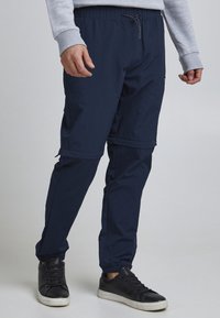 Joggers légers bleu marine avec taille élastique et cordon de serrage. Caractéristiques : fermetures éclair aux chevilles et poche latérale discrète. Texture de tissu lisse.