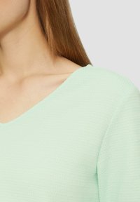Mündroheline tekstuuriga topp, millel on lai ümmargune kaelus, alusel on peen vahvli sarnane muster ja lühikesed varrukad.