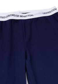 Tmavě modré kalhoty s elastickým pasem, s bílým pruhem nesoucím černý nápis "UNITED COLORS OF BENETTON". Měkká, hladká tkanina.