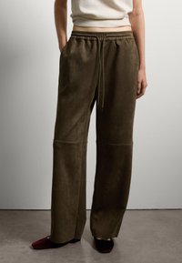 Olivenfarbene, weiche Wildlederhosen mit einem elastischen Bund und einem Kordelzug. Sie haben weit geschnittene Beine und seitliche Taschen.