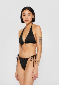 Ensemble bikini noir avec texture côtelée, comportant un haut triangulaire à bords volantés et des liens réglables sur les côtés du bas.
