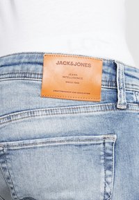 Jeans de mezclilla con un lavado azul claro, parche de cuero con el logotipo de la marca y diseño clásico de cinco bolsillos con costuras en contraste.