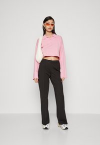 Pink cropped long-sleeve polo shirt with buttons, paired with black tailored pants and white sporty sneakers. Includes a light-colored crossbody bag.