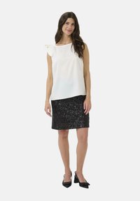 Haut blanc sans manches avec un détail en nœud à l'épaule, associé à une jupe crayon noire en sequins. Le mannequin porte des chaussures à talons noires.