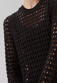 Maglione nero lavorato a maglia caratterizzato da un design a rete aperta con colletto a girocollo a coste e maniche lunghe. Tessuto testurizzato con ampi fori.
