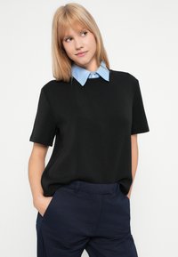 Černý krátký rukávový top s světle modrým límečkem na knoflíčky; hladká textura, volný střih a kulatý výstřih. Spárováno s námořnickými kalhotami.