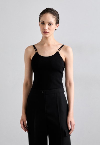 Haut débardeur noir à côtes avec bretelles fines et accents en métal doré, associé à un pantalon noir ajusté avec fermeture à boutons et poches.