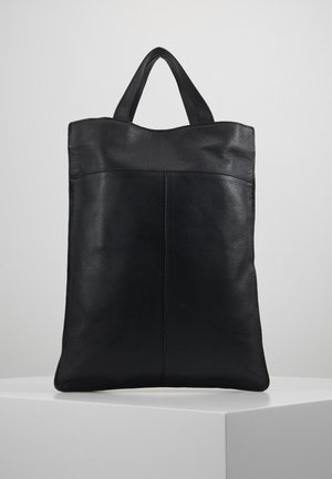 Sac cabas en cuir noir avec deux poignées courtes, forme rectangulaire et coutures visibles, debout sur une surface blanche sur fond gris.
