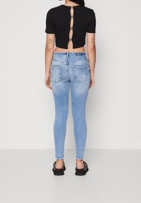 Top corto negro con mangas cortas y detalles de botones en la parte posterior, combinado con jeans ajustados azul claro que presentan un dobladillo deshilachado.