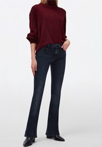 Tummansiniset leveälahkeiset farkut yhdistettyinä viininpunaisiin neulepuseroon, jossa on korkea kaulus. Farkut ovat slim fit -malliset, joissa on sileä pinta ja klassinen tyyli.
