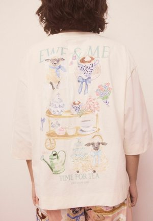 Cremefarbenes, übergroßes T-Shirt aus Baumwolle mit bunten Illustrationen von Schafen, Teetassen und Blumen, mit dem Text "EWE & ME TIME FOR TEA."