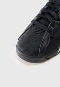 Scarpa sportiva nera realizzata in materiali scamosciati e in rete, dotata di suola in gomma, punta arrotondata e design con lacci, con dettagli neon discreti.