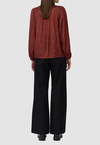 Bordeauxblauwe blouse met lange mouwen, voorzien van geplooide details en verzamelde schouders, gedragen met zwarte jeans met een brede pijp en stevige zwarte laarzen.