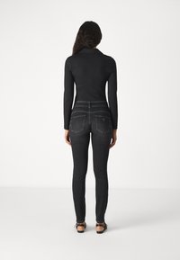 Un haut noir à manches longues et un jean skinny gris foncé, avec des poches avant et arrière, des coutures minimales et un design ajusté. Des sandales plates complètent le look.