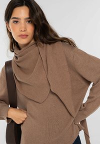 Suéter marrón con escote drapeado y parte delantera en capas. Presenta textura acanalada y mangas largas. Combinado con un bolso de hombro marrón.