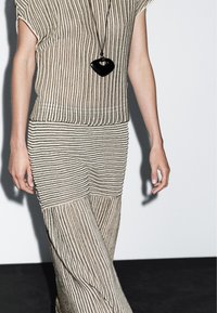Gestreiftes Strickoberteil und Rock in Beige und Schwarz, mit lockeren Ärmeln, lässiger Passform und einem langen, fließenden Design. Accessoires mit einem schwarzen Anhänger.