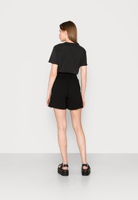 T-shirt en coton noir à manches courtes, associé à un short noir à taille élastique. Modèle portant des sandales à plateforme noires, de dos par rapport à l'appareil photo.