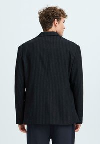 Black pinstriped blazer with a notched collar, structured shoulders, and a relaxed fit. The fabric appears textured and tailored.