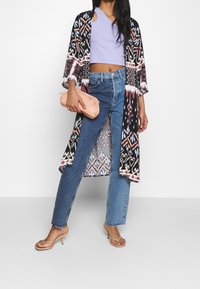 Długi czarny kimono z kolorowym, wzorzystym zdobieniem, zestawiony z jasnofioletowym topem typu crop i niebieskimi dżinsami z wysokim stanem. Różowa torebka kopertowa i sandały.