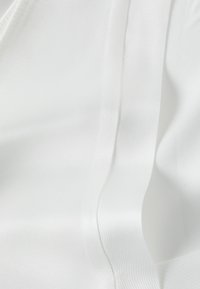 Tissu satin blanc présentant une texture lisse et brillante avec de douces plis et un subtile éclat, mettant en valeur l'apparence luxueuse du matériau.