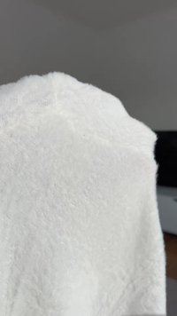 Weißes Handtuch mit einer weichen, plüschigen Textur, das eine dreieckige Form aufweist und eine detaillierte Naht entlang der Kanten hat.