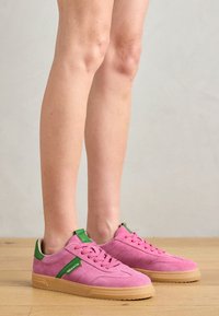 Pink suede sneakers with green accents, featuring a textured surface, lace-up design, and a gum sole.