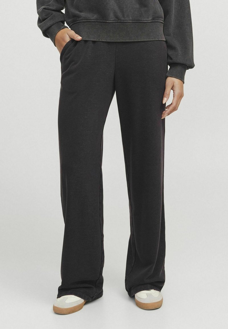 Schwarze Sweatpants mit einem entspannten Schnitt, ausgestattet mit Seitentaschen und einer glatten Texture, kombiniert mit hellen Turnschuhen.