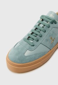 Light blue suede sneaker with smooth leather accents, round toe, flat laces, and a gum rubber sole. Features gold logo detailing.