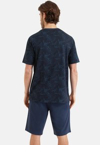 Chemise à manches courtes bleu marine avec un motif de feuilles, vue de dos, associée à un short bleu marine. Tissu doux, coupe décontractée, sans équipement visible.