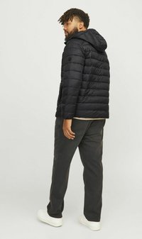 Sort pufferjakke med hætte, der har en quiltet design og lynlås-lommer i siderne, båret med mørke bukser og hvide sneakers.