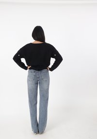 Schwarzer Pullover mit abgesenkten Schultern, gerippten Bündchen und kleinen goldenen Akzenten, kombiniert mit hochtaillierten, hellblauen, weiten Jeans.