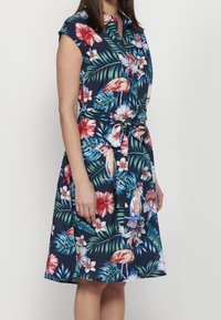 Blumenkleid mit navyfarbenem Hintergrund, das bunte Hibiskusblüten und tropische Blätter zeigt. Beinhaltet einen Kragen und einen Taillengürtel zur Formgebung.