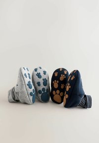 Grå och marinblå toffelsockar med gummipaw prints på sulorna; grå har teal detaljer, marinblå har brunt. Randig tyg synlig på en socka.